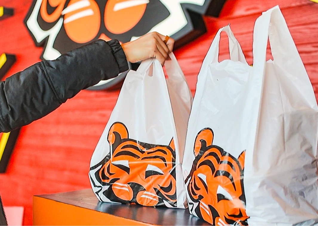 entrega un pedido en bolsa con el logo del tigre dentro del restaurante.